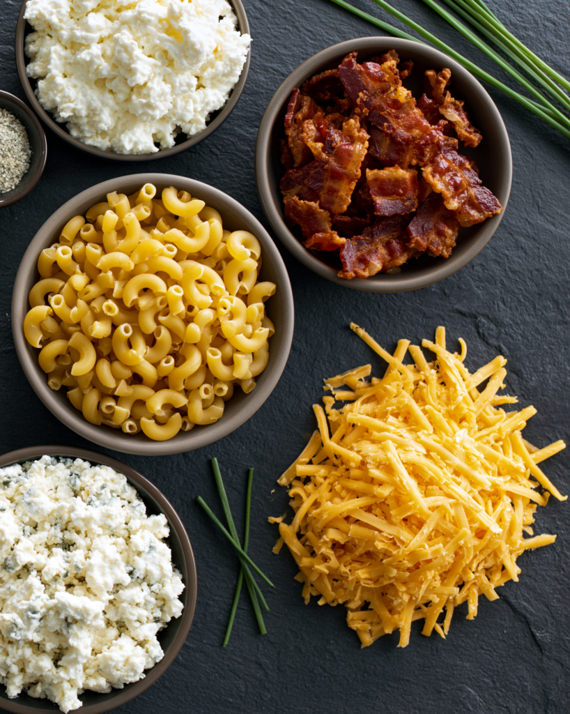 Flat lay of bacon ranch mac and cheese ingredients: macaroni, cottage cheese, bacon, ranch seasoning, cheddar