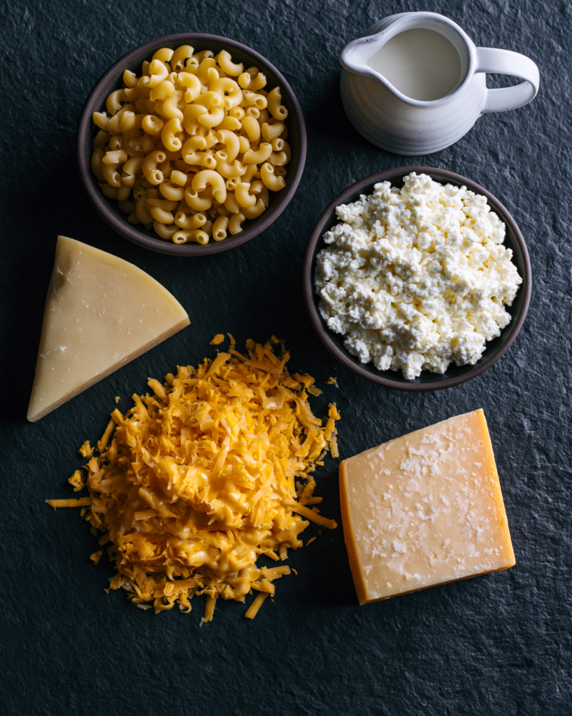 Flat lay of three cheese mac and cheese ingredients: macaroni, cottage cheese, cheddar, gruyere, parmesan
