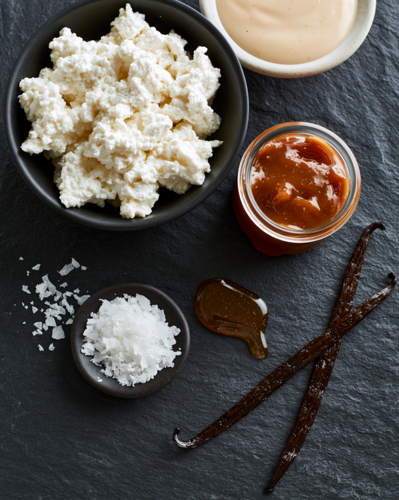 Flat lay of cottage cheese snack board components: cottage cheese, honey, crackers, berries, grapes, seeds