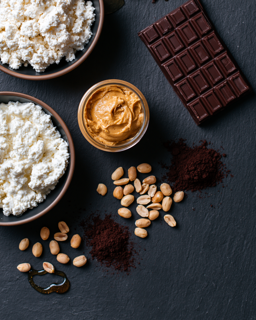 Flat lay of peanut butter chocolate mousse ingredients: cottage cheese, peanut butter, dark chocolate, cocoa, peanuts