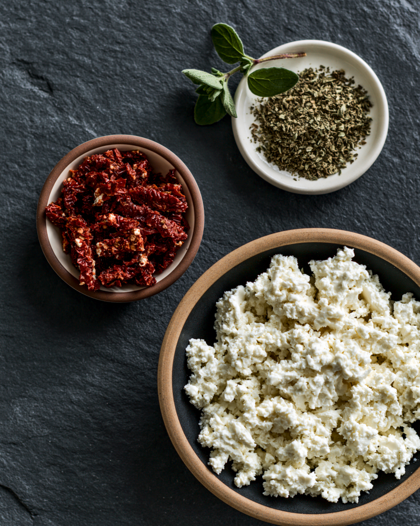Flat lay of sun-dried tomato cottage cheese chips ingredients: cottage cheese, sun-dried tomatoes, oregano